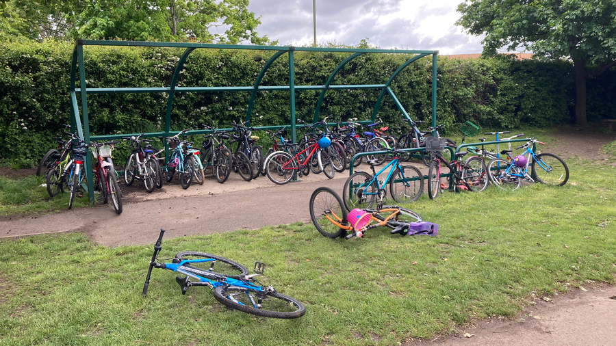cycle rack with overflow bikes attached to edges of frame and lying on the grass