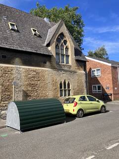 green half-cylinder cycle hangar with small yellow car next to it