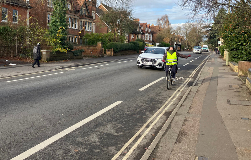 road with cycle lanes on either side, a person is cycling towards the photographer, with a car in the central lane not far behind them